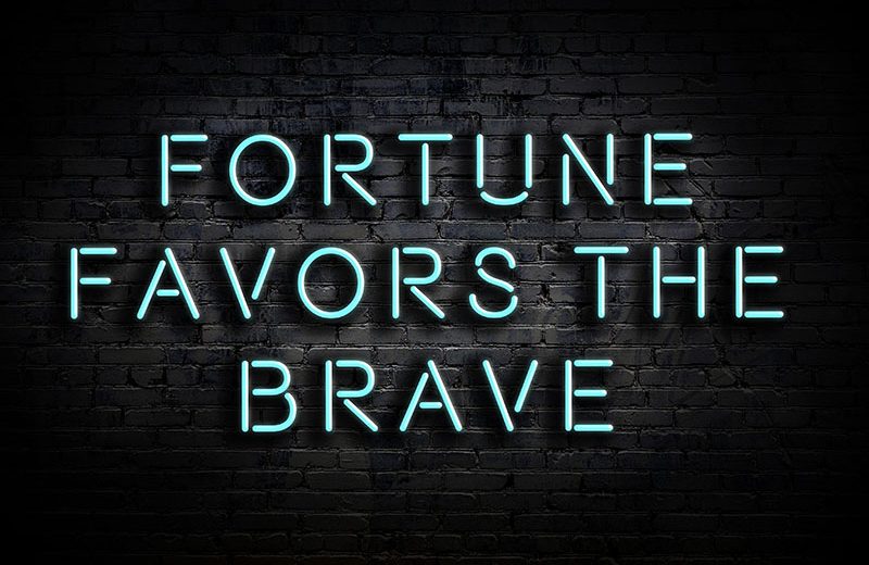 Fortune favors the brave blue text on black brick wall