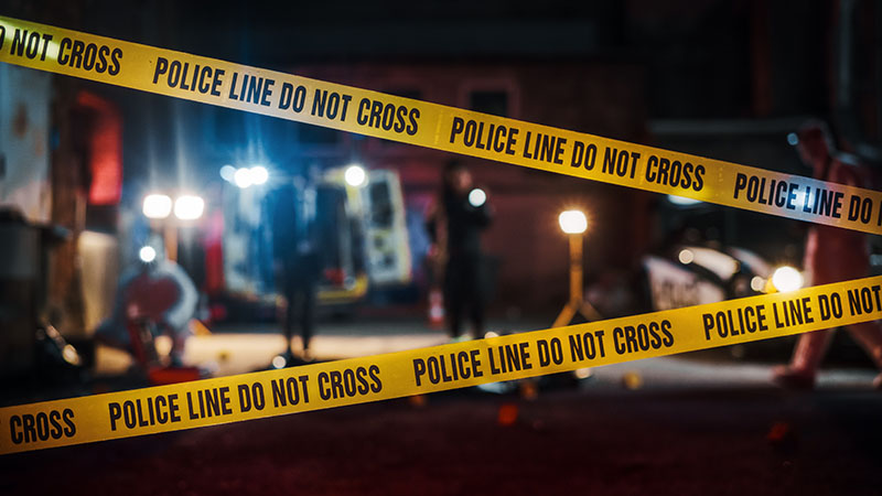 Two police line tapes block a crime scene setting at night